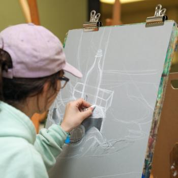 Student drawing a still life with white chalk on gray paper during an art class.