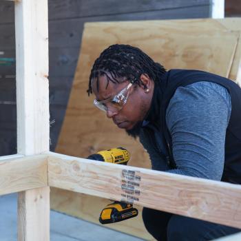 Construction student wearing safety glasses uses a drill to assemble a wooden frame.
