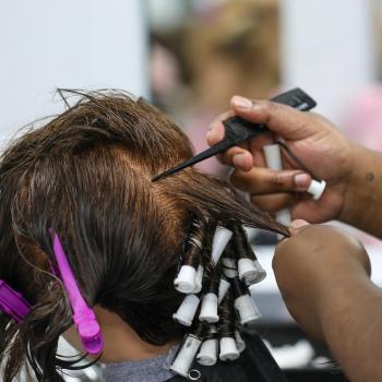 Cosmetology student wraps sections of a mannequin’s hair around perm rods.