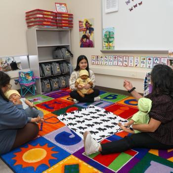 Early childhood education students practice infant care with baby dolls in a classroom.