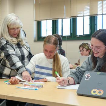 Instructor assists two students working together on an assignment in a classroom.