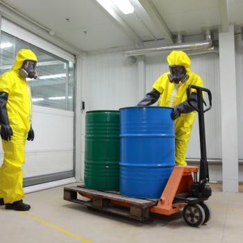 Safety students wearing hazardous-material protective suits and respirators work with industrial drums.