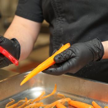 Culinary student wearing gloves peels a carrot during food preparation.