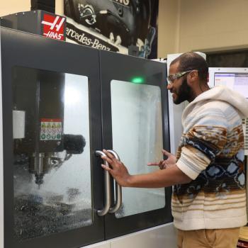 Manufacturing student wearing safety glasses operates a CNC milling machine.