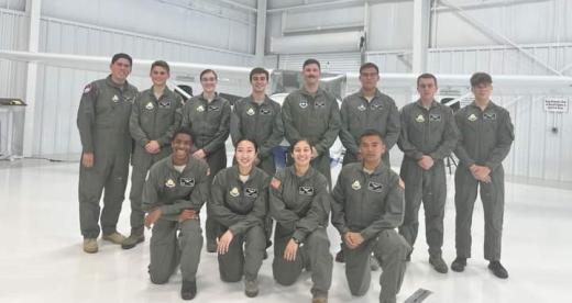 Twelve students in flight school camp pose in the hangar wearing flight suits