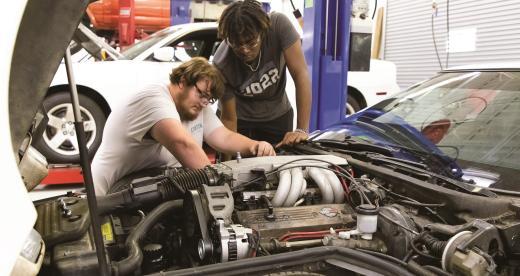 Two male students in the Automotive program work on a car