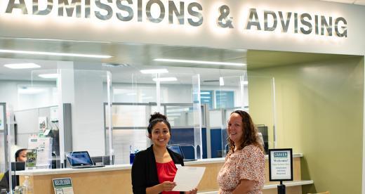A Craven CC staff member and student smile outside the Admissions & Advising counter