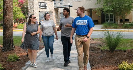 Two females and two male students walking outside on path with Craven CC entrance sign in background