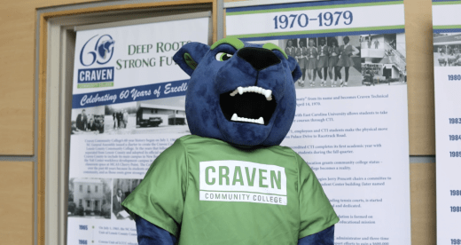 Blaze the panther blue and green mascot in front of college's 60th anniversary banners