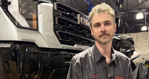 Automotive Systems Technology graduate Adam Heckman stands in front of a suspended car in the shop