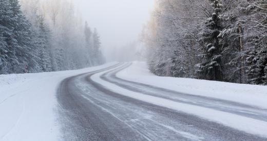 Icy road lined with snowy ground and trees