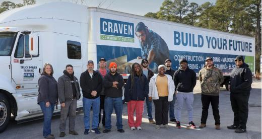 group of people standing in front of white truck with trailer