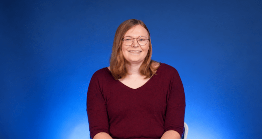 Woman wearing red shirt sits in front of blue background