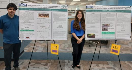 Two students stand with poster projects