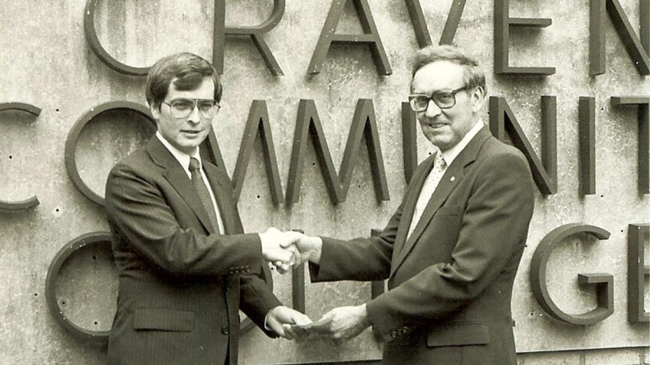 Craven CC's founding president, Dr. Thurman Brock, shakes a man's hand and accepts a check in front of the Craven sign in the 1960s