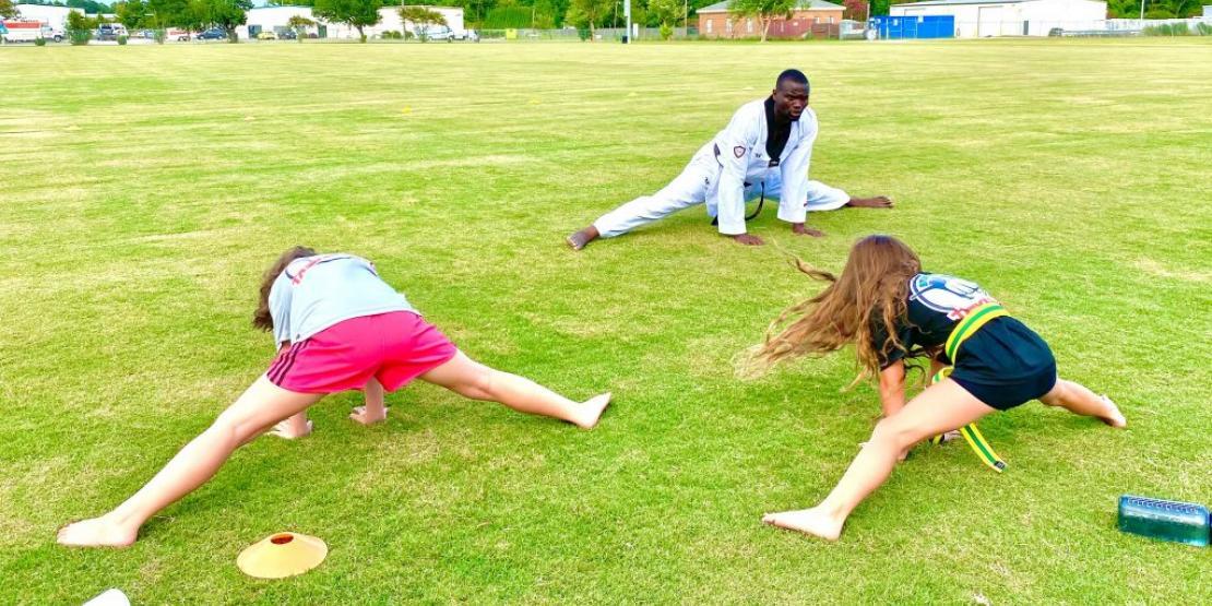 Taekwondo instructor and students stretching outside on grass