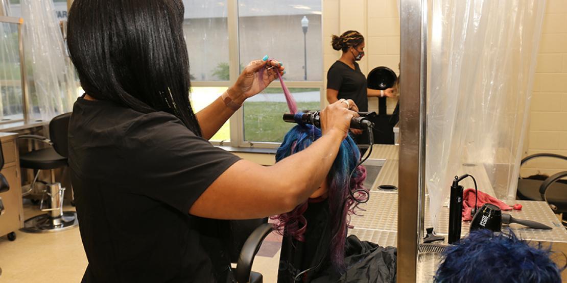 cosmetology student practices curling hair on wig