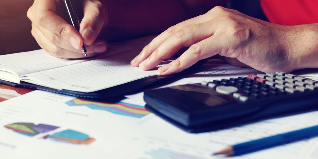 Person writing with calculator and graph data