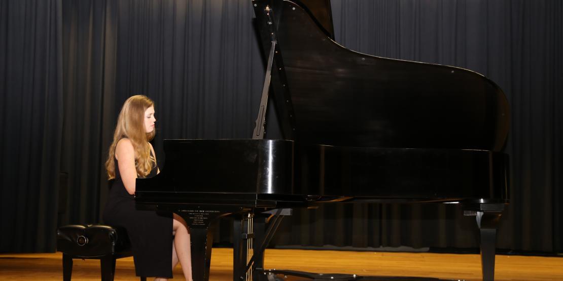 Woman in black dress plays black baby grand piano on stage