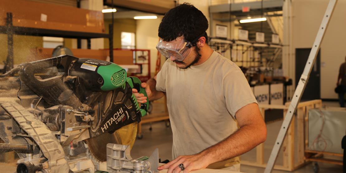 Male student in safety goggles cuts wood with table saw