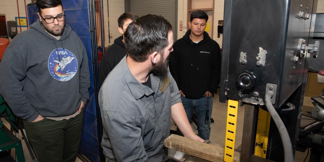 An instructor shows a group of students how to work a machine