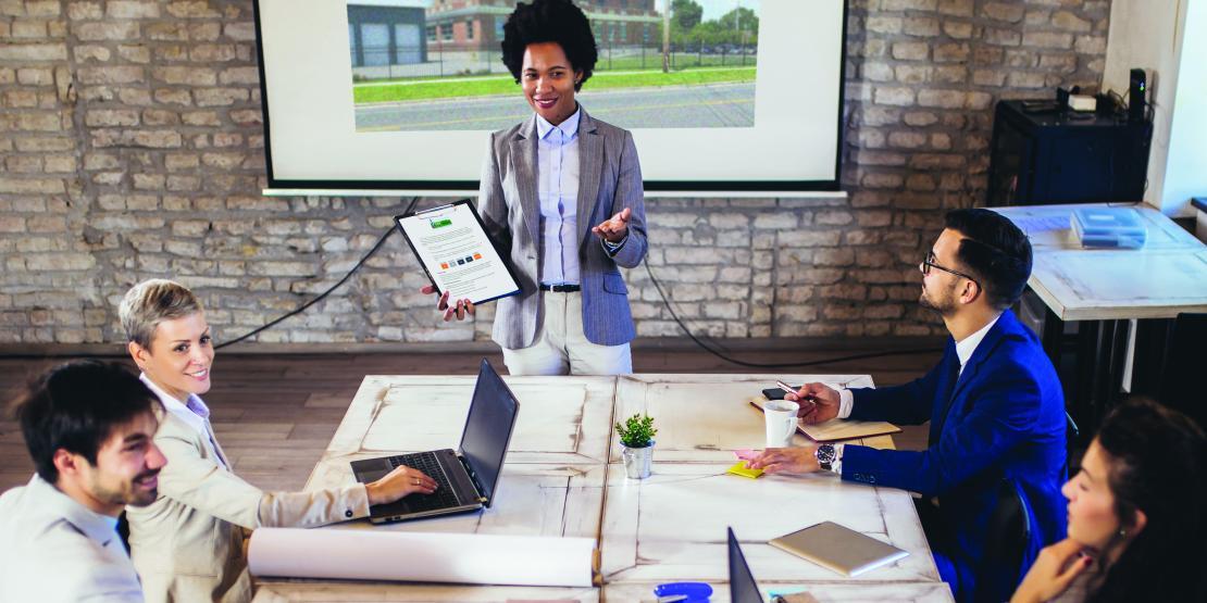 Woman gives business presentation in front of conference table of people