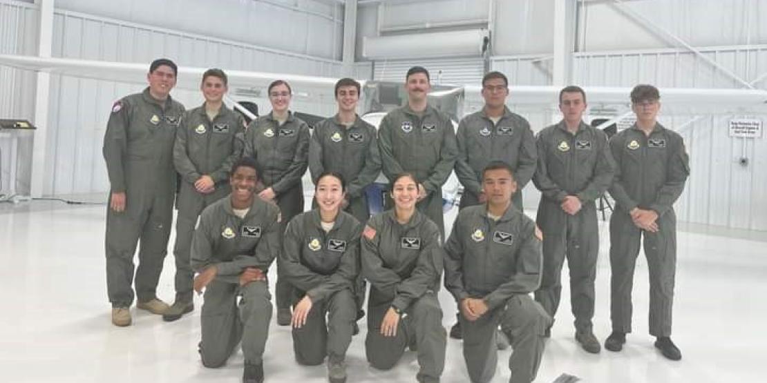 Twelve students in flight school camp pose in the hangar wearing flight suits