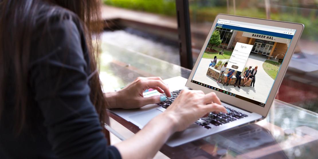 girl with long brown hair and blue nails sits in front of laptop with Craven CC Self-Service page open