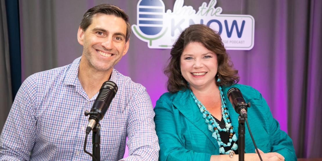 Craig Ramey and Megan Johnson pose in front of In the Know podcast sign