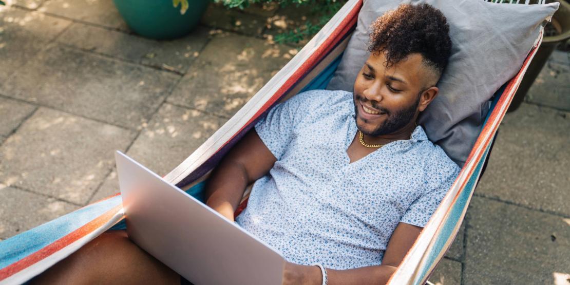 Male student with laptop relaxes in hammock outside