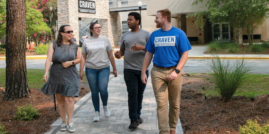 Two females and two male students walking outside on path with Craven CC entrance sign in background