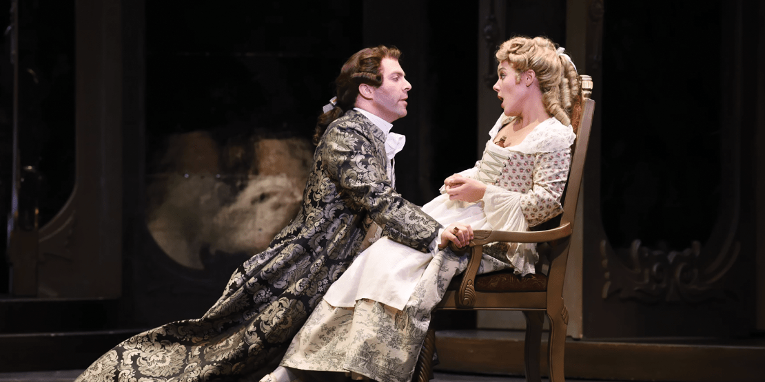 Male actor in 19th century garb kneeling and reaching out to female actress in white dress sitting in chair