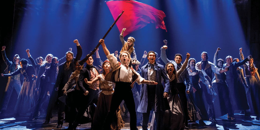 Cast of Les Miserables prepared for battle with one person holding a red flag