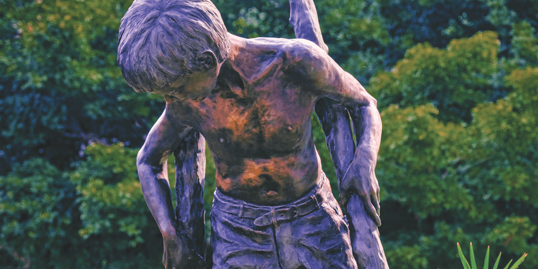 Bronze statue of young shirtless boy on stilts