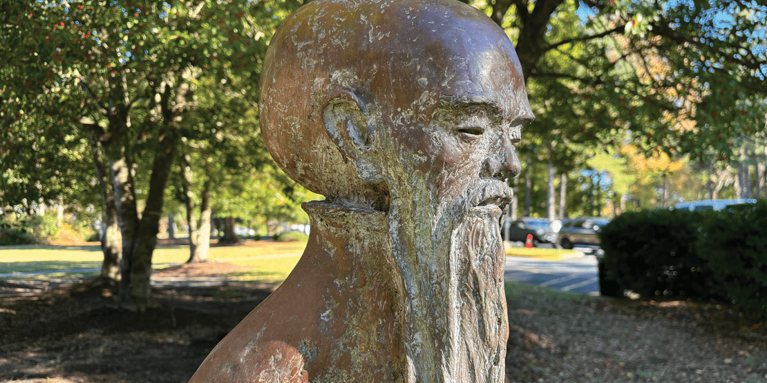 Bronze statue of old Asian man with long beard and mustache