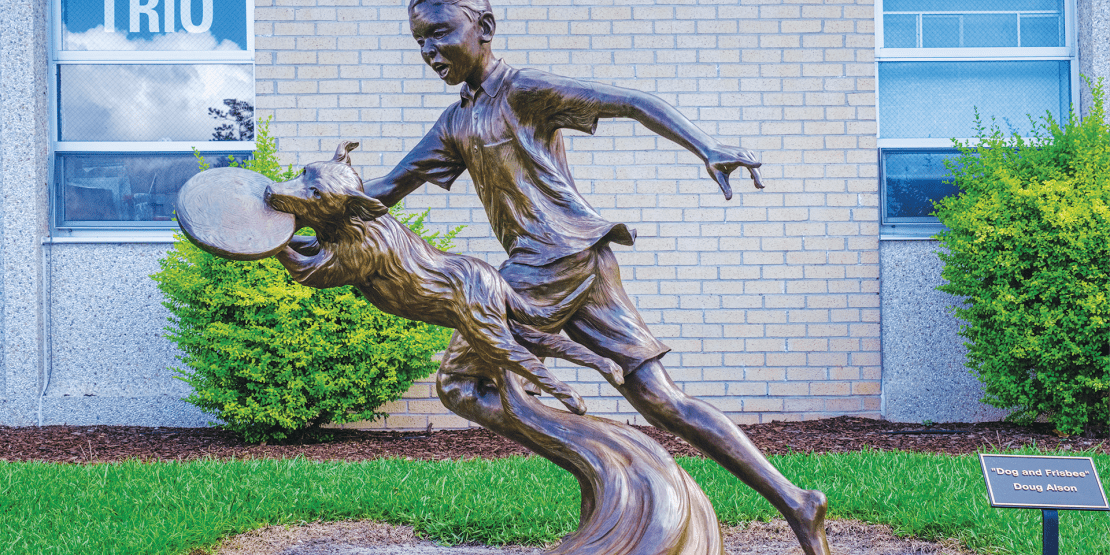 Bronze statue of boy and dog with frisbee