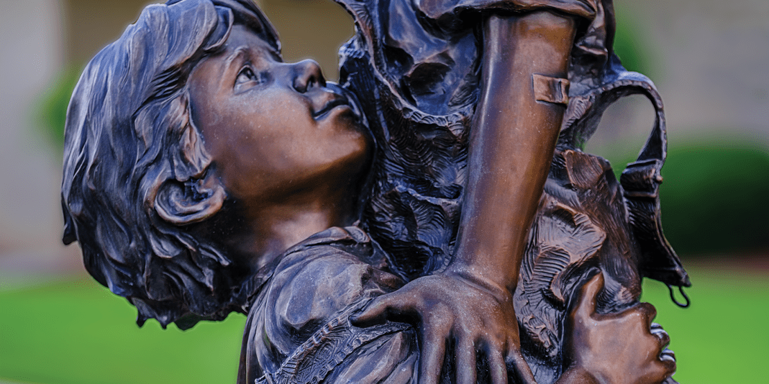 Bronze statue of boy lifting up girl to get an apple