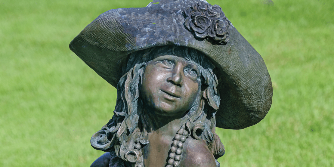 Bronze statue of little girl dressed in her mother's hat, shoes, and pearls