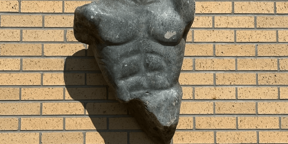 Granite sculpture of a male torso on brick exterior wall