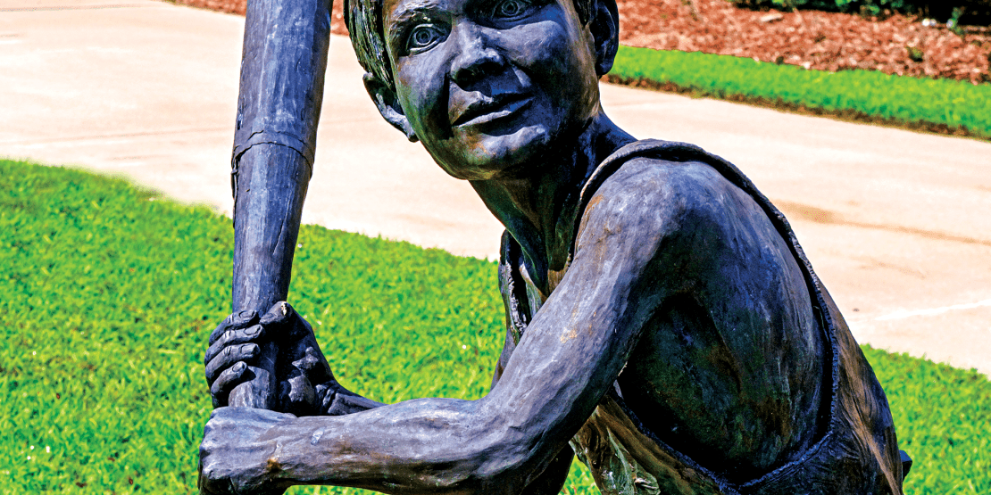 Bronze statue of little boy in overalls swinging a baseball bat