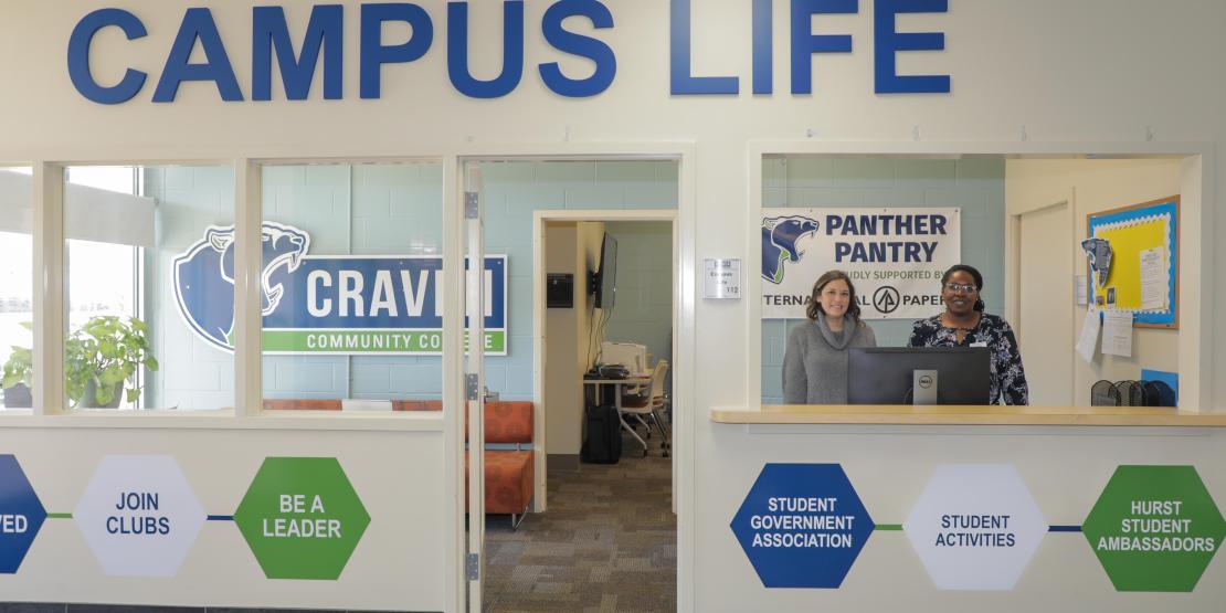 Two female employees stand in window of Craven's Campus Life department