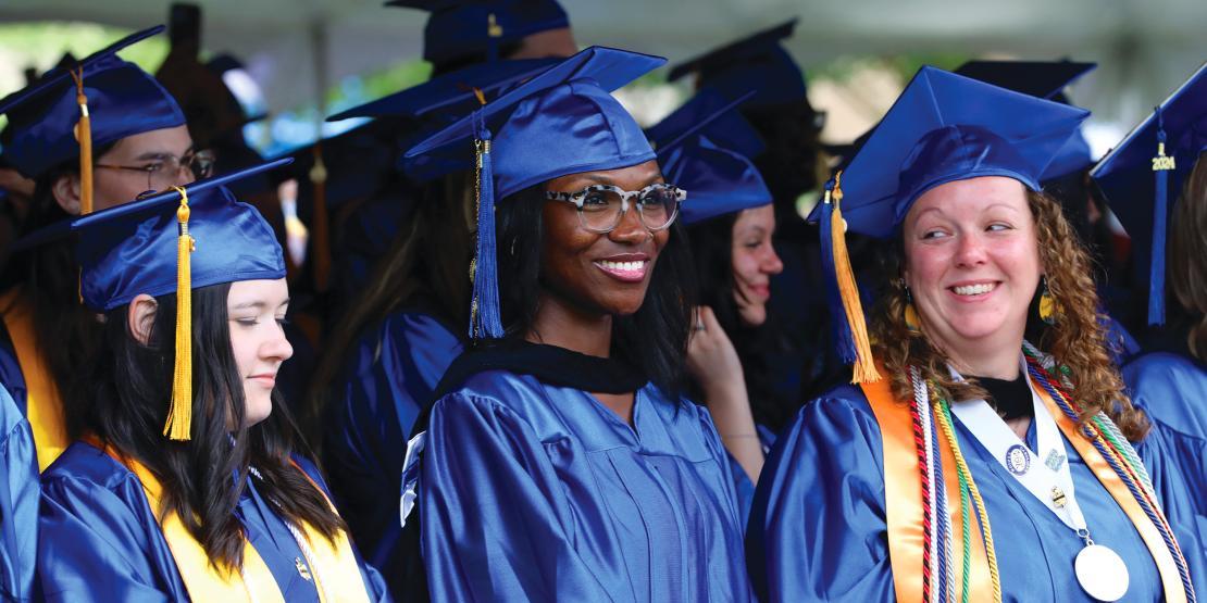 Group of graduates in caps and gowns smile during graduation day 2024.