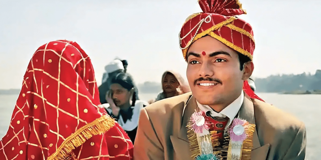 Hindi bride covered in red and gold checkered veil travels with male in turban