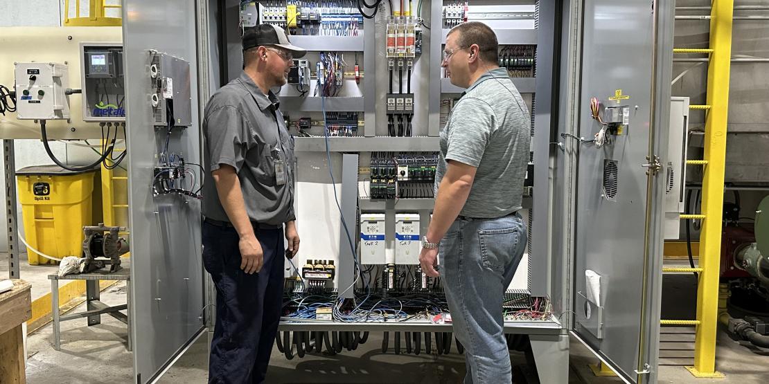 Chatsworth employees Cody Marshall and Stephen Calabro stand in front of an industrial control panel