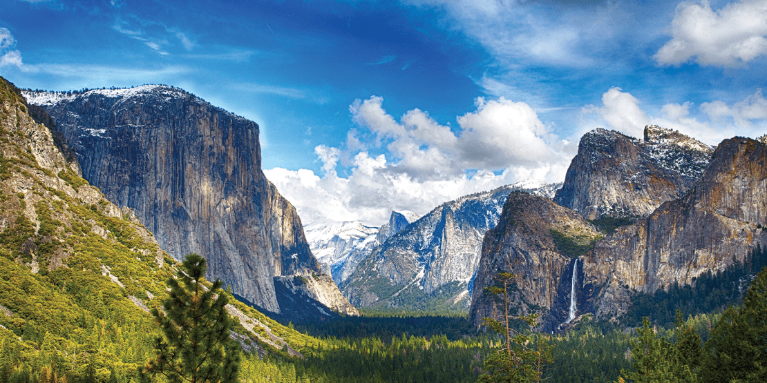 Picturesque view of mountains, hills of pine trees and greenery, and cloudy blue sky