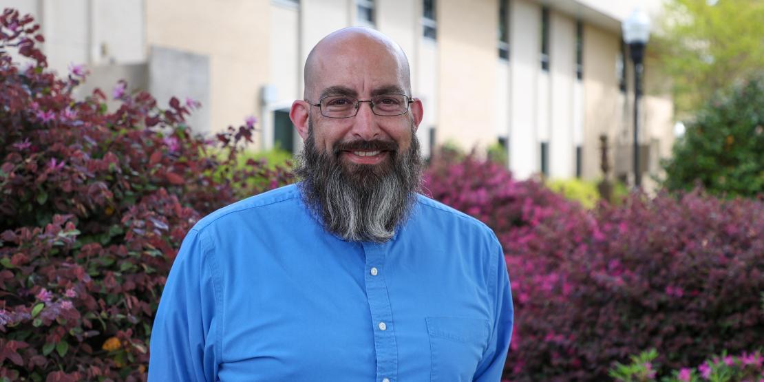 Man with beard stands smiling outside