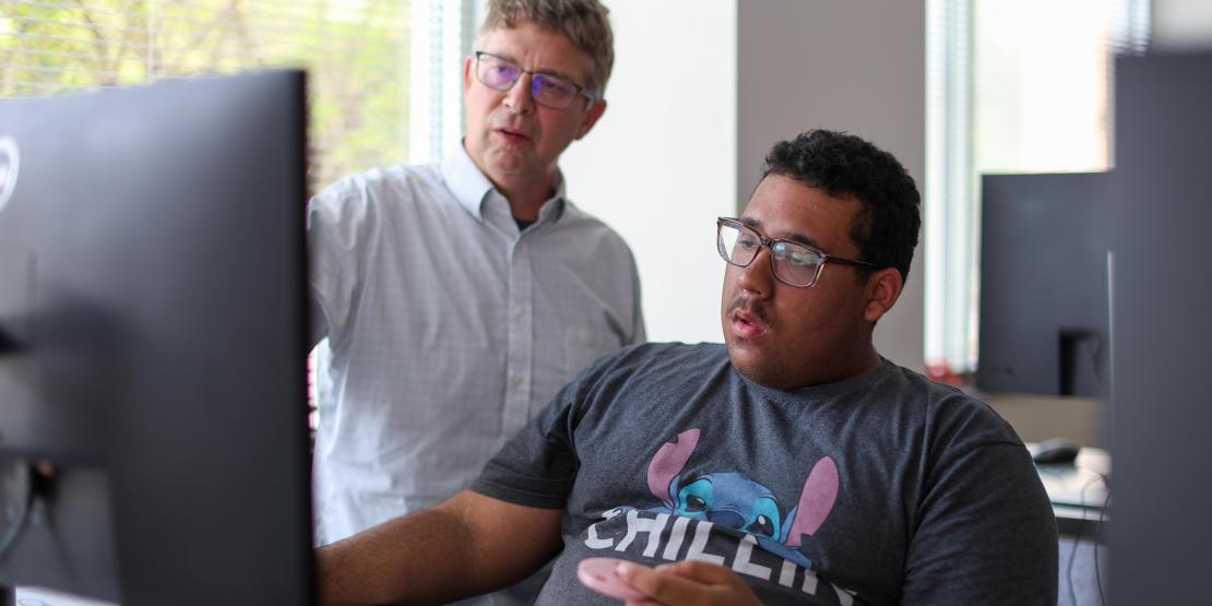 Student sitting at computer with instructor helping