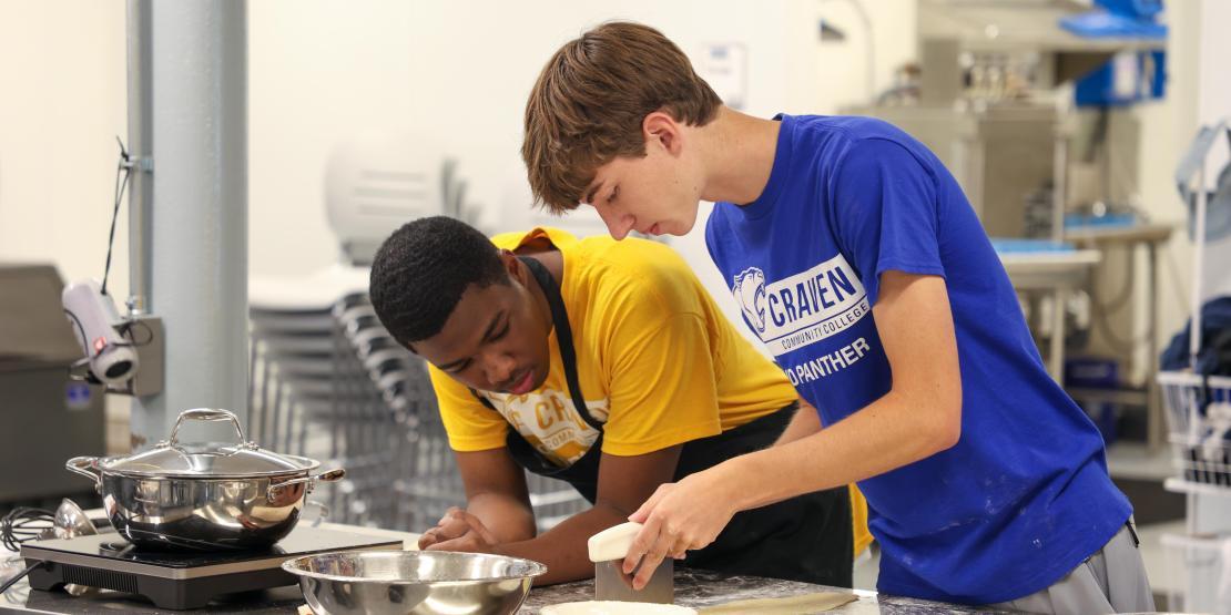 Two male students measure ingredients in a kitchen