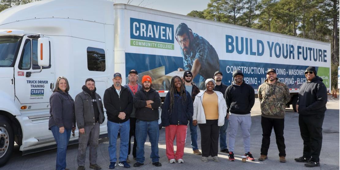 group of people standing in front of white truck with trailer