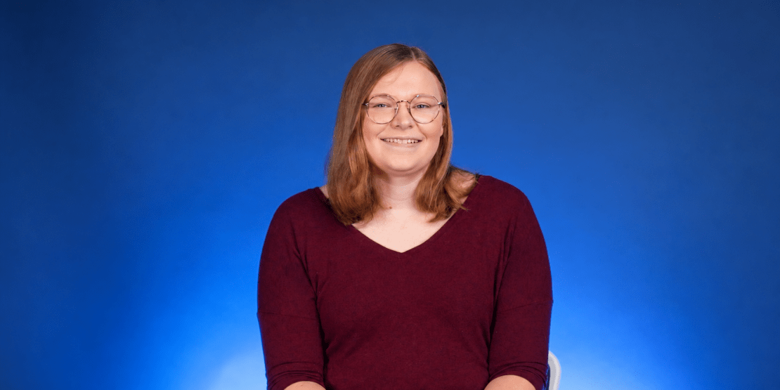 Woman wearing red shirt sits in front of blue background